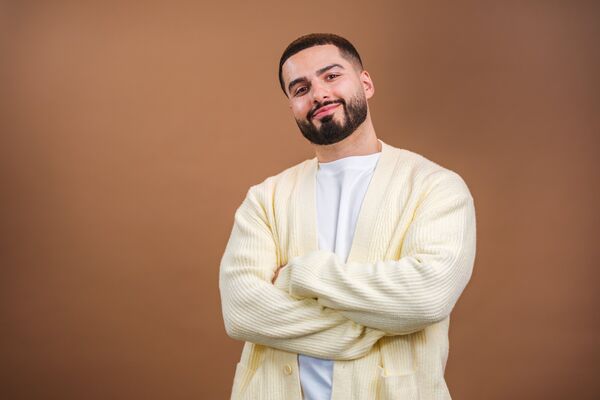 Kae Kurd wearing a pale yellow cardigan with his arms crossed