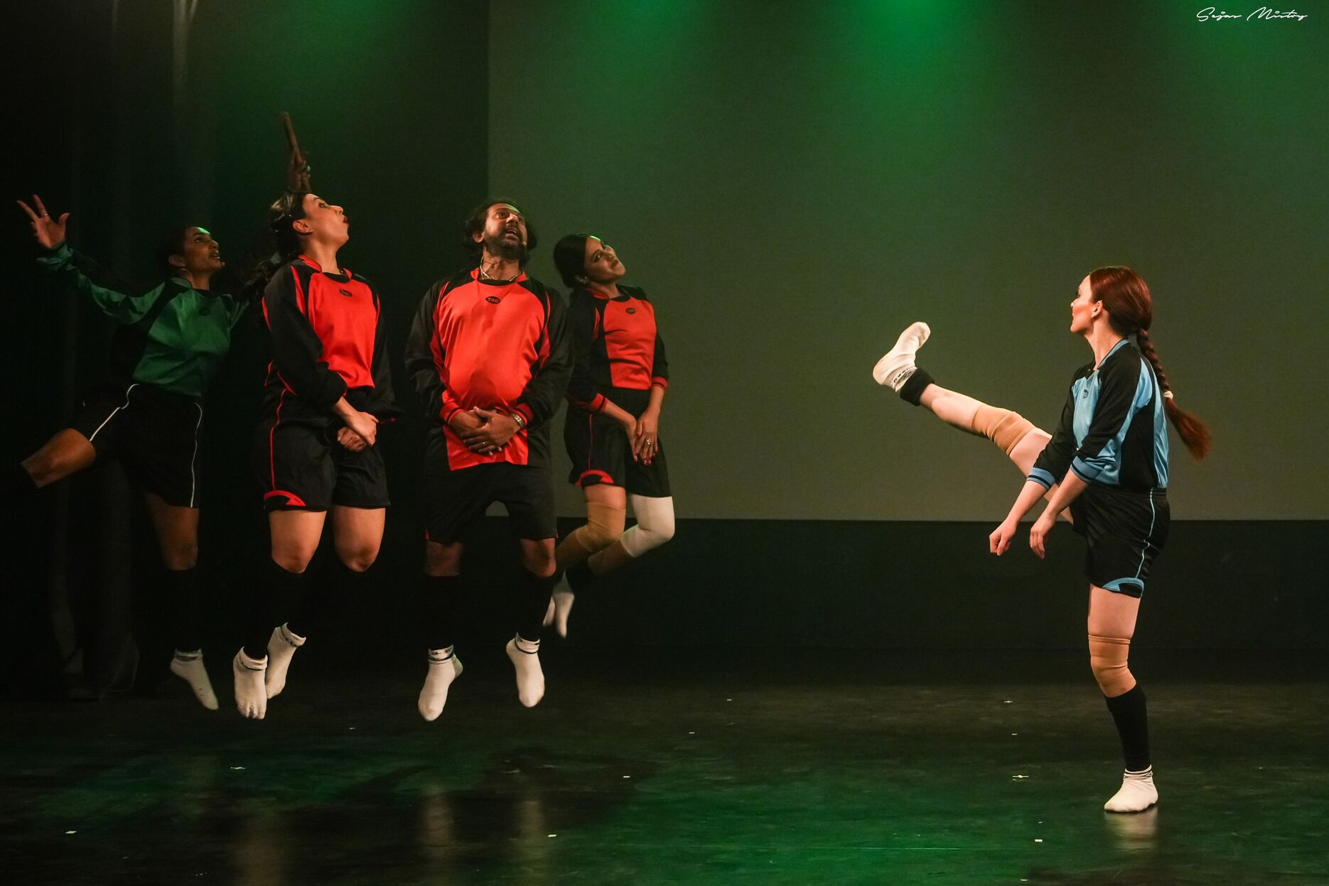 Woman mimicking kicking a ball with 4 people in a wall jumping