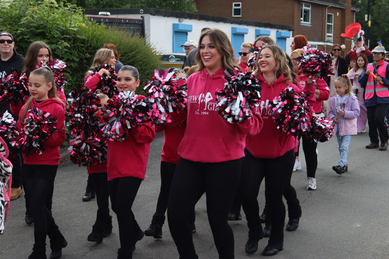 A group of dancers wearing matching bright pink hoodies and holding black and pink pom-poms perform in the street during the Canley Parade 2025.