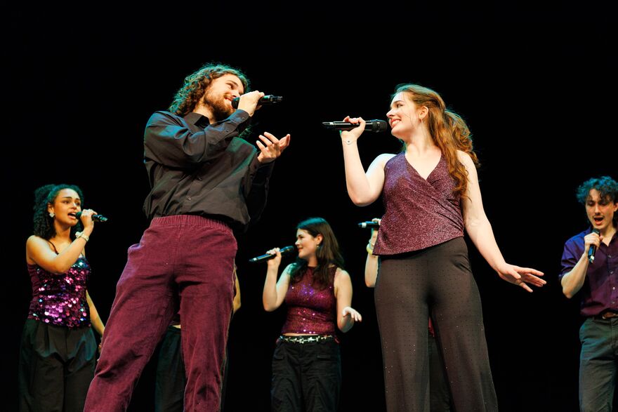 5 people singing holding microphones