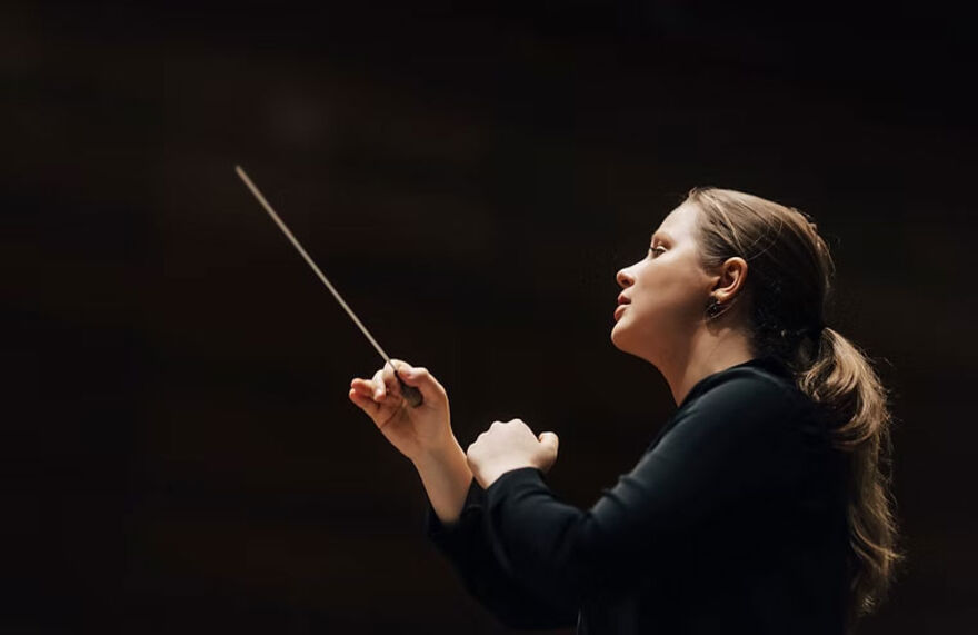 A woman conducting against a black background