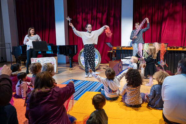 Children and parents sat on floor watching 3 performers 