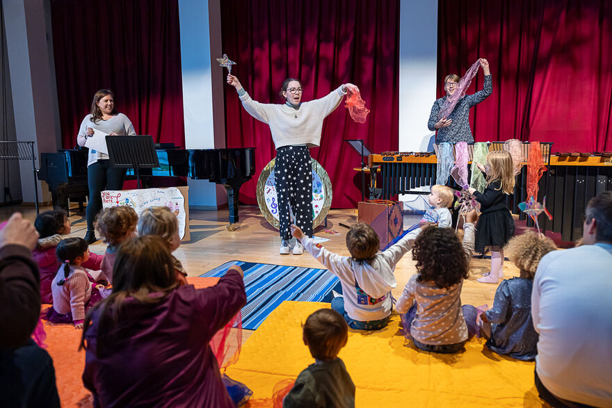 Children and parents sat on floor watching 3 performers 