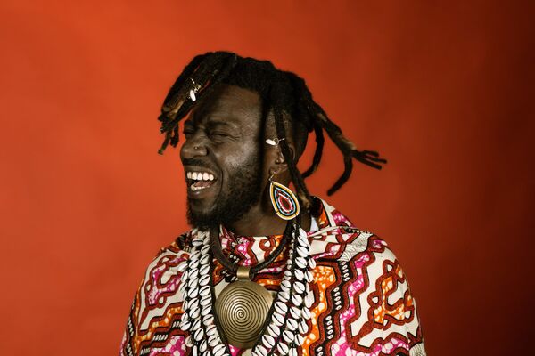 Kweku Sackey in colourful earrings, a colourful shirt and large necklace 