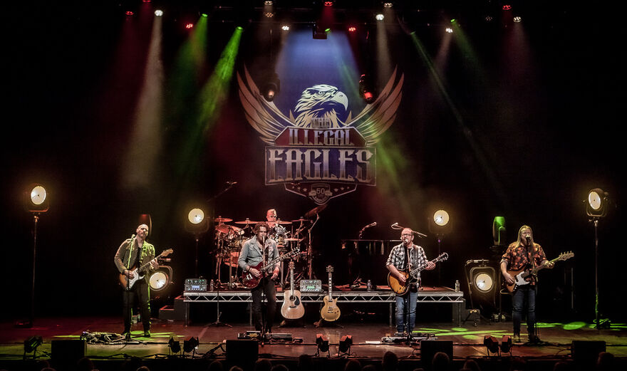 4 musicians on stage with 'Illegal Eagles' banner behind them