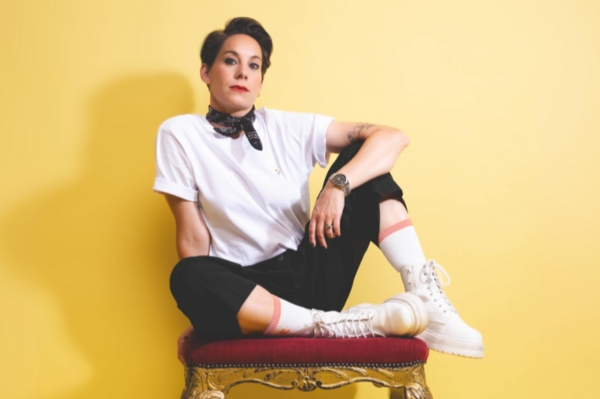 Suzi Ruffell sitting on a red chair in front of a yellow background