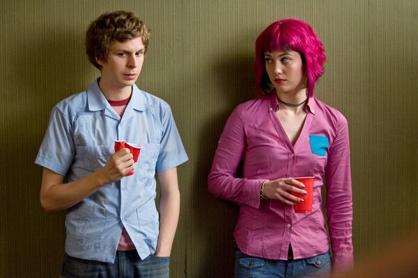 A teenage boy stands anxiously next to a teenage girl with bright pink hair. A teenage boy stands anxiously next to a teenage girl with bright pink hair.
