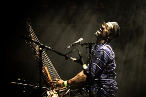 Seckou Keita smiling holding a Kora with mkicrophone in fornt of him