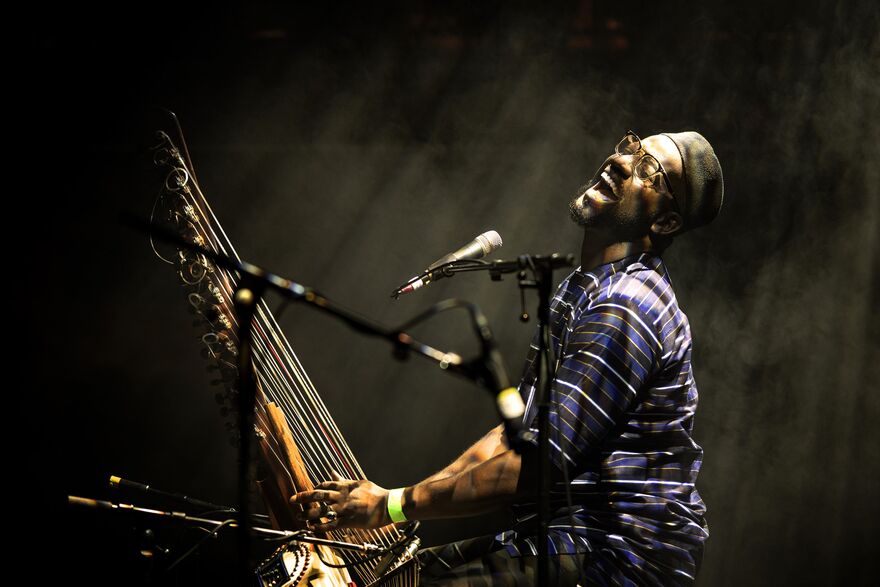 Seckou Keita smiling holding a Kora with mkicrophone in fornt of him