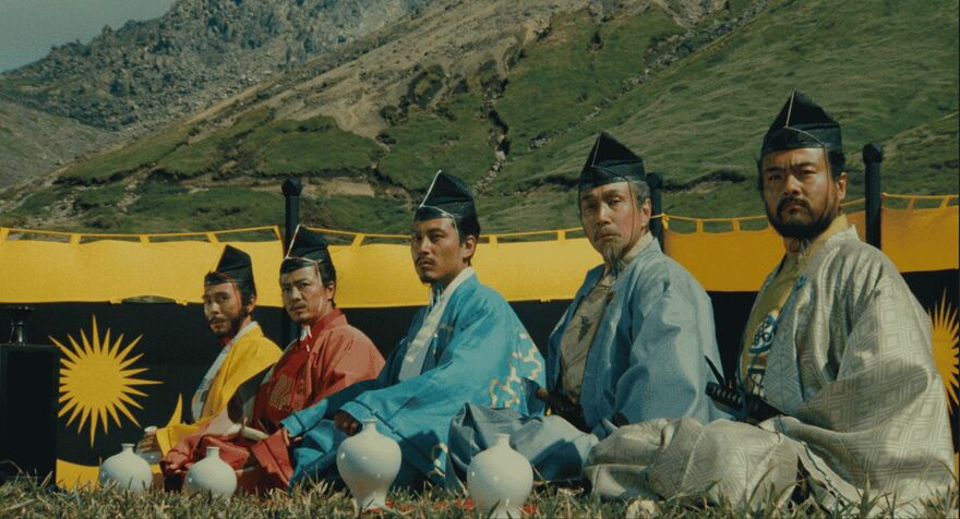 Five men in traditional Japanese dress sit in a line in front of a hillside. 