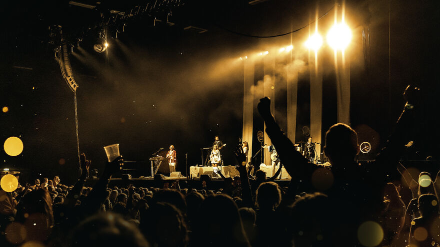 Four musicians stand on a stage before a large crowd