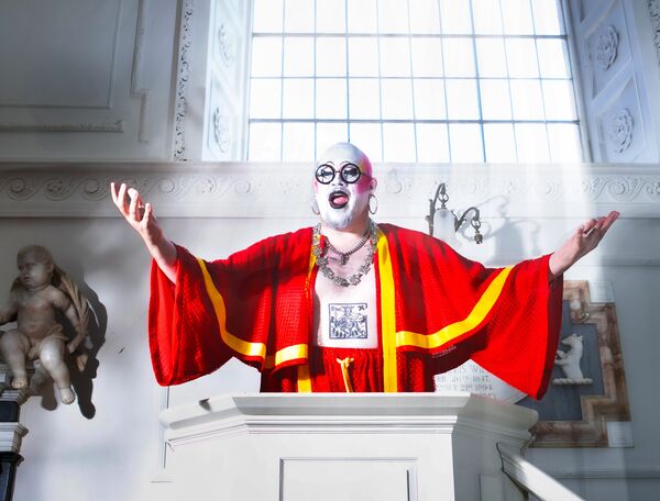 Fatt Butcher in white make up in a red choir robe behind a lectern Fatt Butcher in white make up in a red choir robe behind a lectern