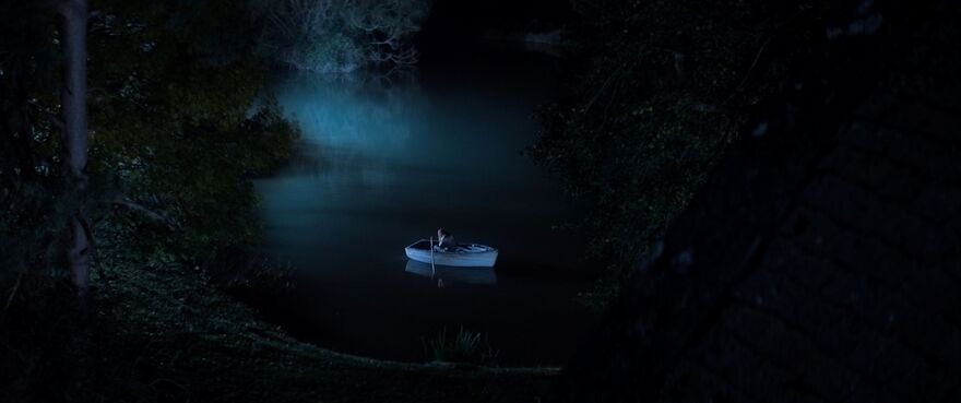 A lone person sits in a rowing boat in the middle of a lake.