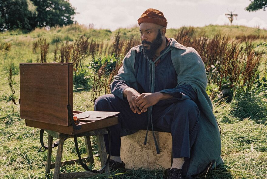 A man sits in a field looking into an open case.