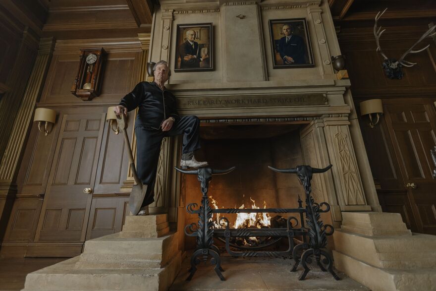 A man holding a shovel stands with one foot on a grand fireplace. 