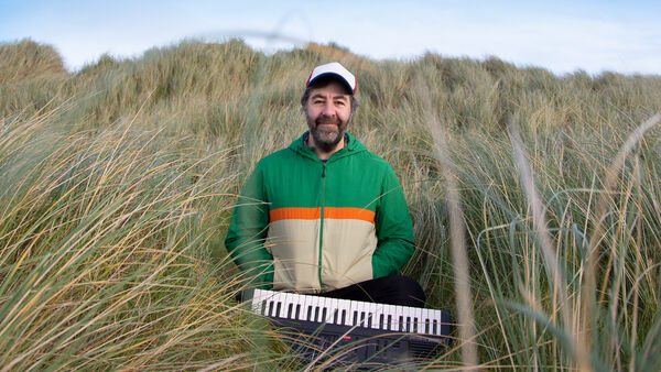 David O'Doherty sitting amongst long grass with a small keyboard