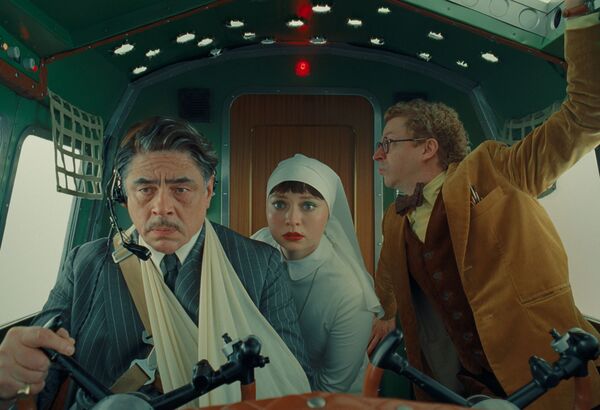 A man in a sling pilots an aircraft. A nun and another man sit beside him looking concerned. 