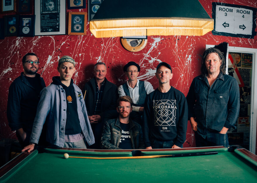 The members of Peatbog Faeries stand in front of a snooker table