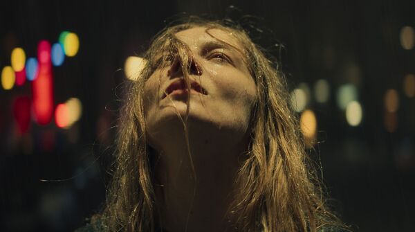 A woman looks up as it rains. 