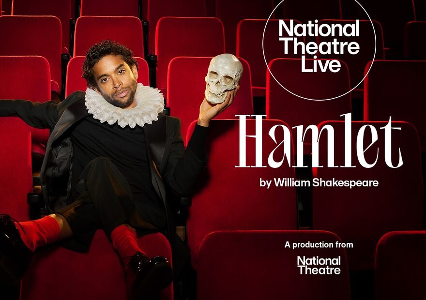 Hiran Abeysekera as Hamlet sitting in a red theatre seat holding a skull. 