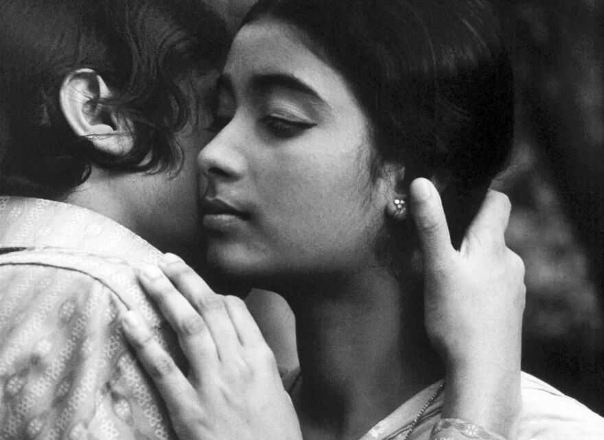 A black and white image of a girl being embraced by another. Her eyes are closed. 