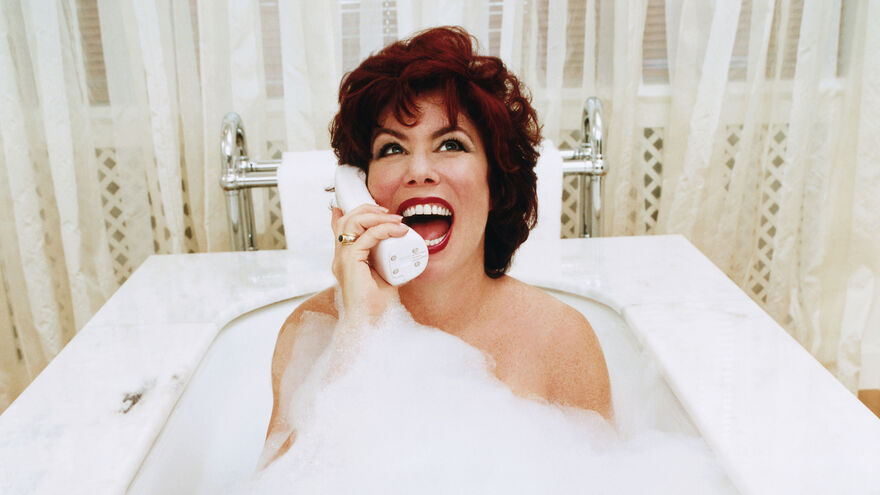 Ruby Wax in a bubble bath smiling on a phone