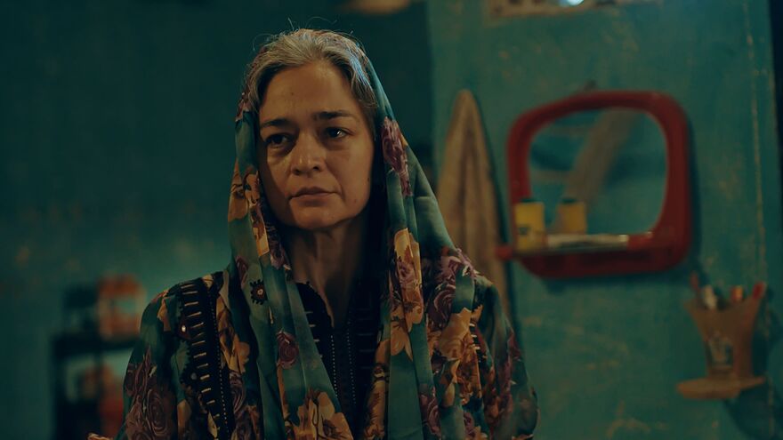 A woman wearing a head covering. She stands in a room with green walls. 