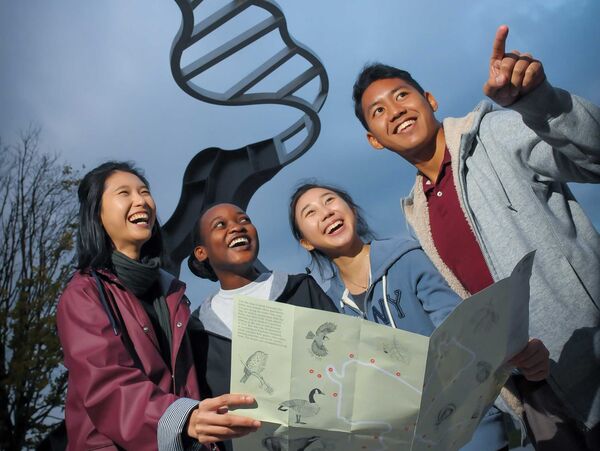 A group of students with a map underneath the Let's Not Be Stupid sculpture