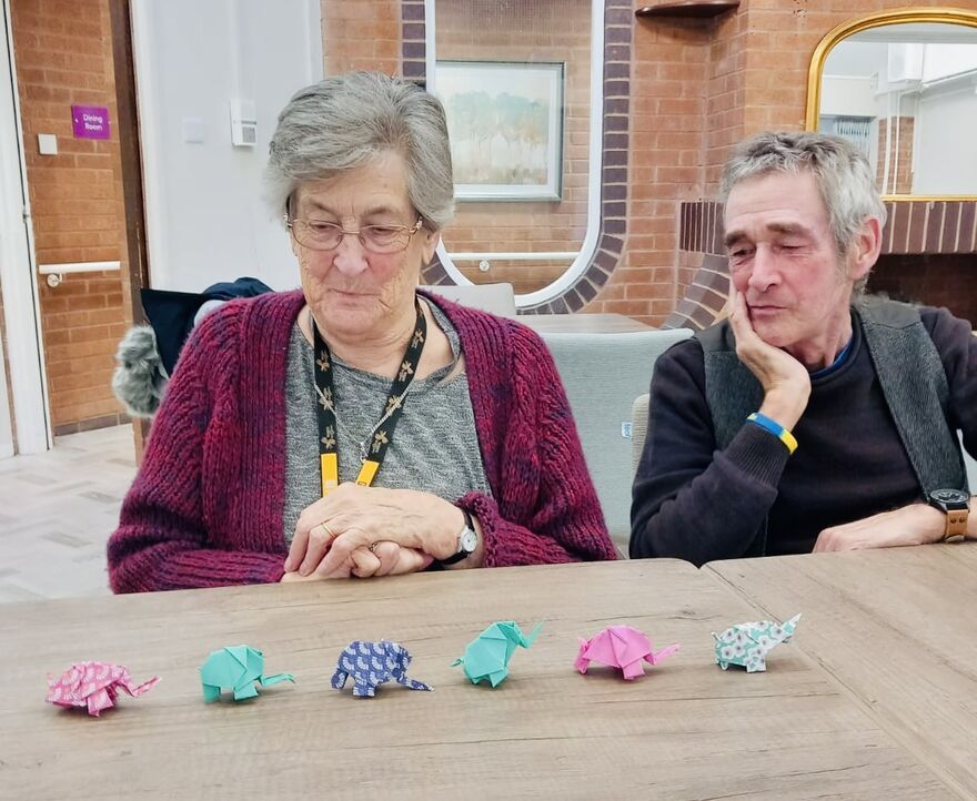Man and woman sitting at a table looking at origami elephants