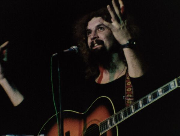Billy Connolly on stage with a guitar. 