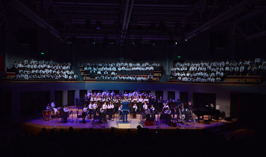 A wide shot of a student choir and orchestra performance in Butterworth Hall.