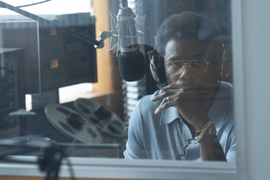 A man sits smoking in a radio sound booth. 