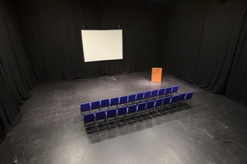 Black Box studio venue with two rows of chairs, a lecturn and a projector screen