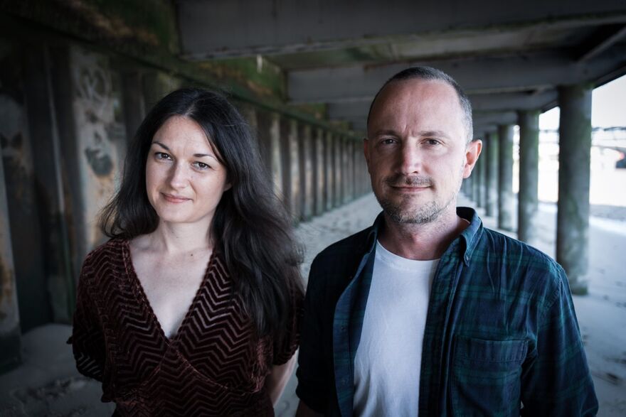 Trish Clowes & Ross Stanley stood under a pier on a beach