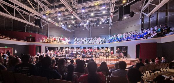 Audience sat down in the foreground, people on stage in the middle of the image and audience sat on balcony seats in the background
