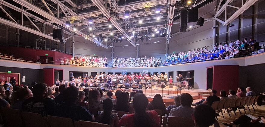 Audience sat down in the foreground, people on stage in the middle of the image and audience sat on balcony seats in the background