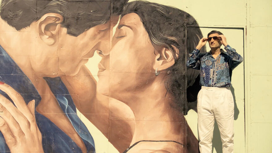 A man in sunglasses stands next to a large wall mural. 