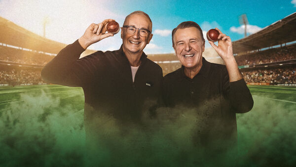 Cricket legends Jonathan 'Aggers' Agnew and Phil 'Tuffers' Tufnell smiling warmly and holding up red cricket balls against the backdrop of a packed, sunlit stadium, with green theatrical smoke rising in the foreground.