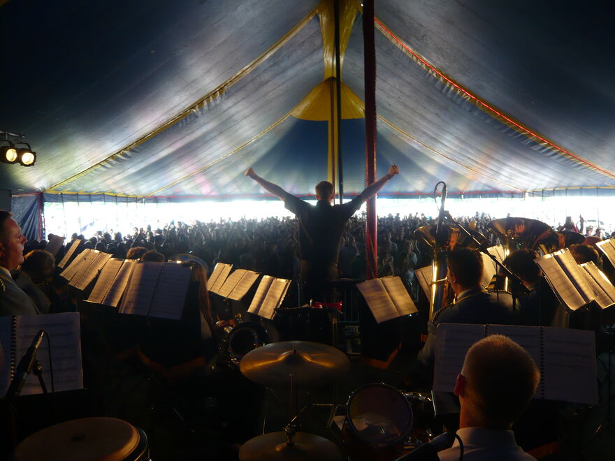 Jeremy Deller performing on stage in a tent backed by brass band