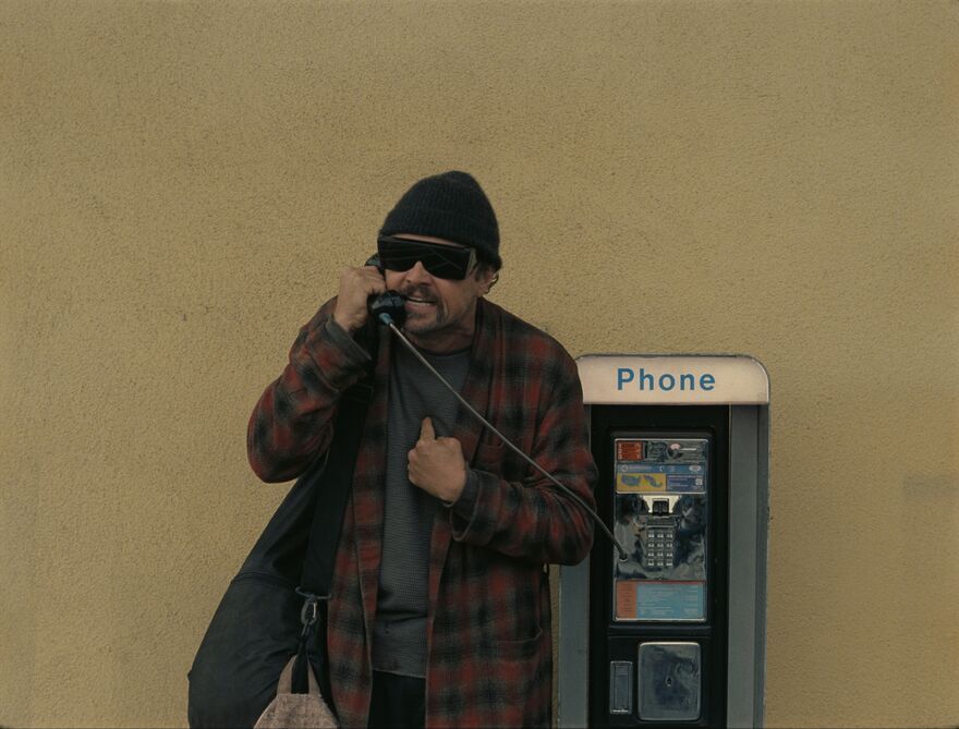 A man with sunglasses and a beanie on a payphone.