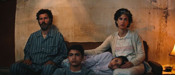 A family of four sit together on a sofa in their pyjamas. 