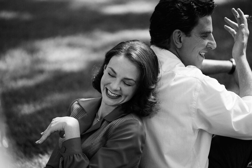 A black and white image of Bradley Cooper and Carey Mulligan as Leonard Bernstein and Felicia Montealegre Cohn. They are sitting back to back laughing.