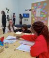 A group of young people sit around a wooden table working with papers and pens in a gallery space.