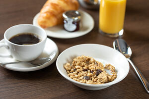 A bowl of cereal, a coffee and a croissant on a wooden table