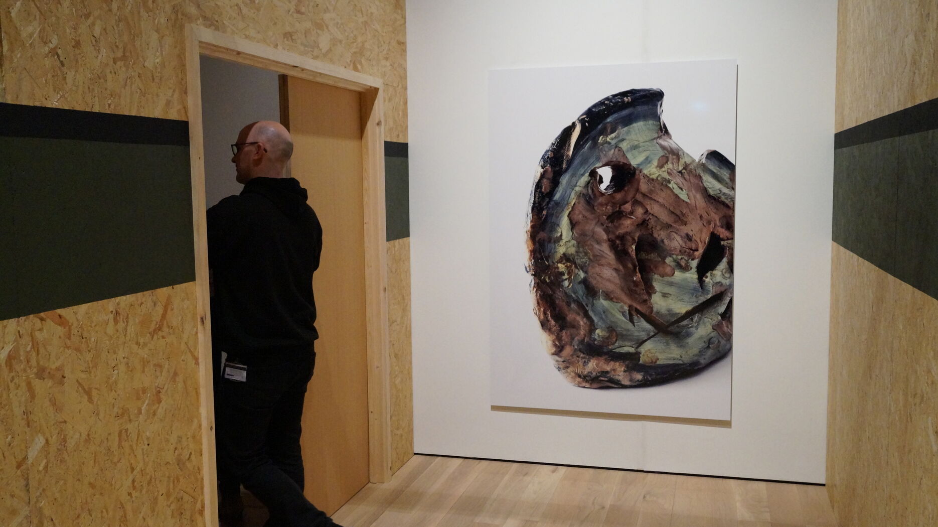 Person walking through a doorway in an exhibition with an artwork on a wall. 