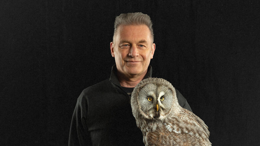 Chris Packham smiling holding an owl