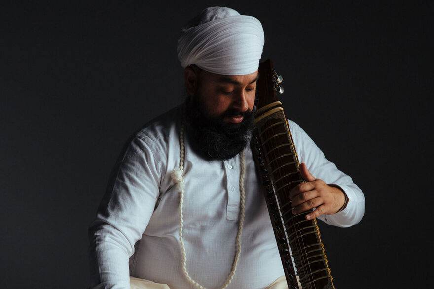 Kirpal sits in on the floor holding a musical instrument