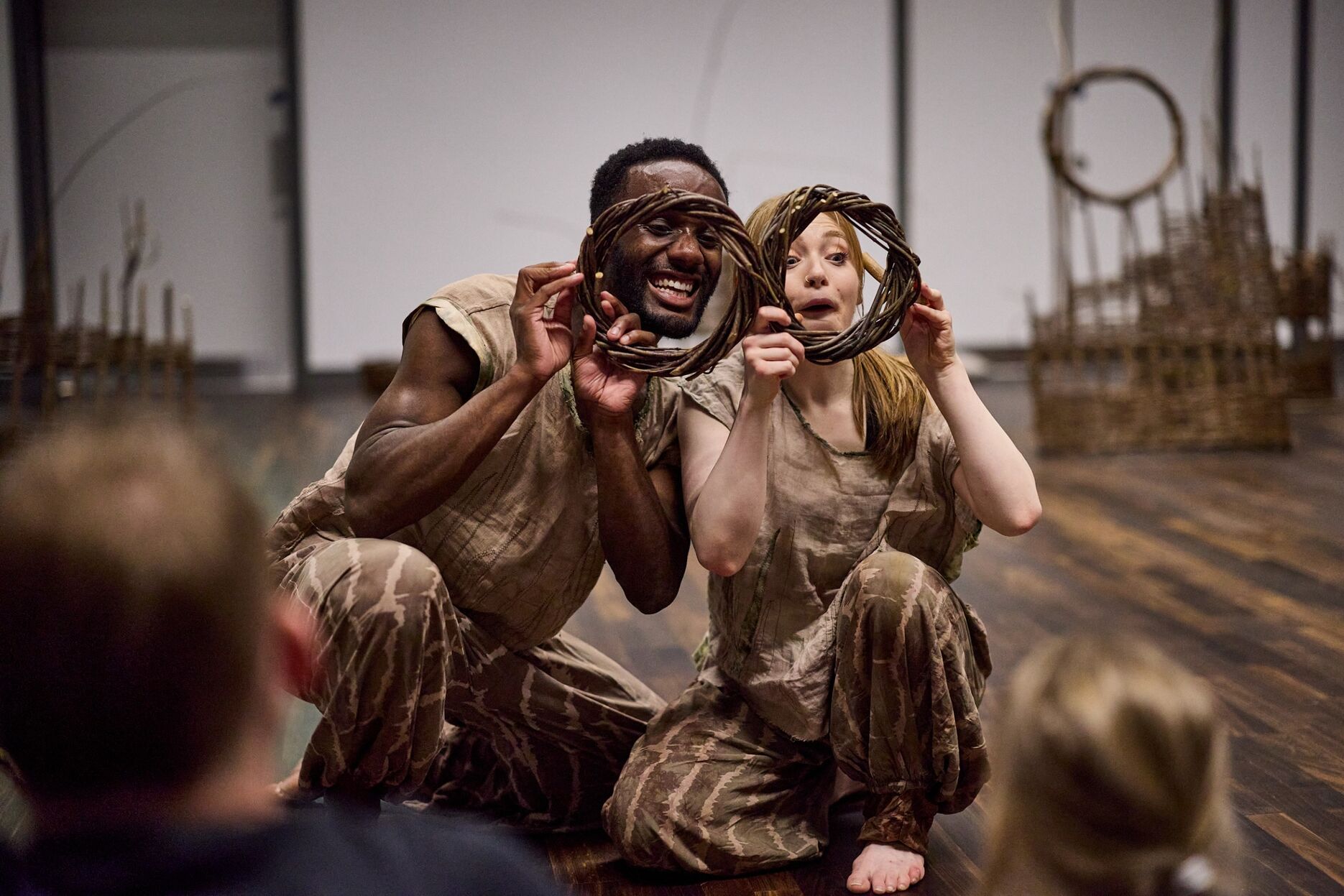 Two dancers kneeling holding weaved circles over face