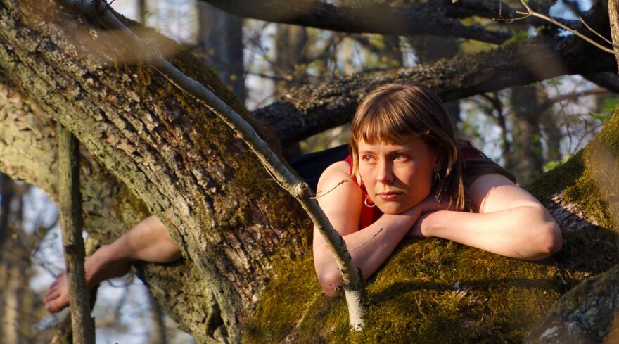 A young woman lies across a large tree branch.