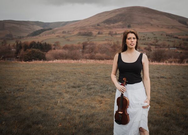 Woman stood in a field holding a violin 